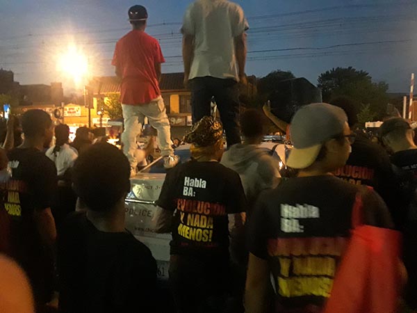 La gente se para en el capó de un coche de policía rodeado de otros que protestan contra el asesinato policial.