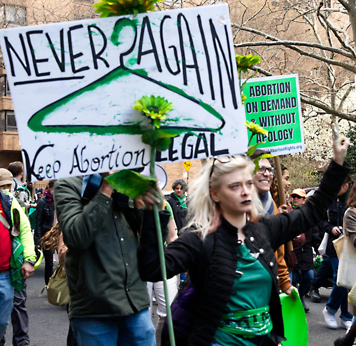 Woman with green coat hanger with sign Never Again at Rise Up 4 Abortion Rights rally in NYC.
