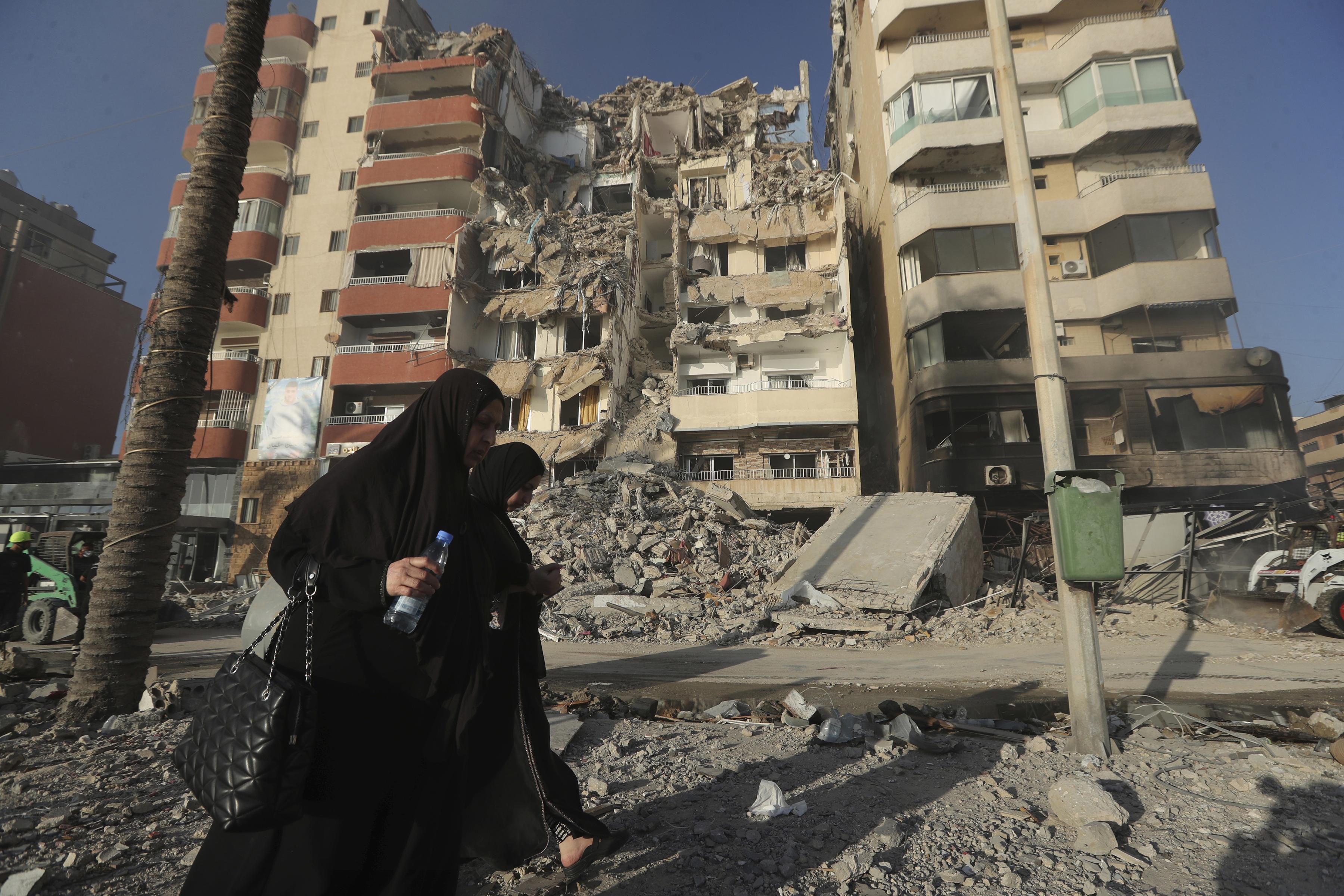 Lebanese women pass in front of a destroyed building hit in an Israeli airstrike in Tyre, Lebanon, Monday, Oct. 28, 2024.