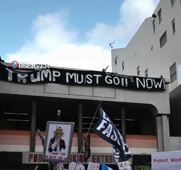 Los Angeles May Day march goes by building with long black banner "Trump Must Go NOW!"