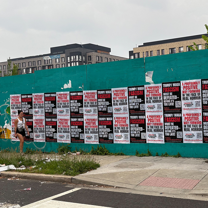 Woman walking by wall covered with BobAvakianOfficial posters.
