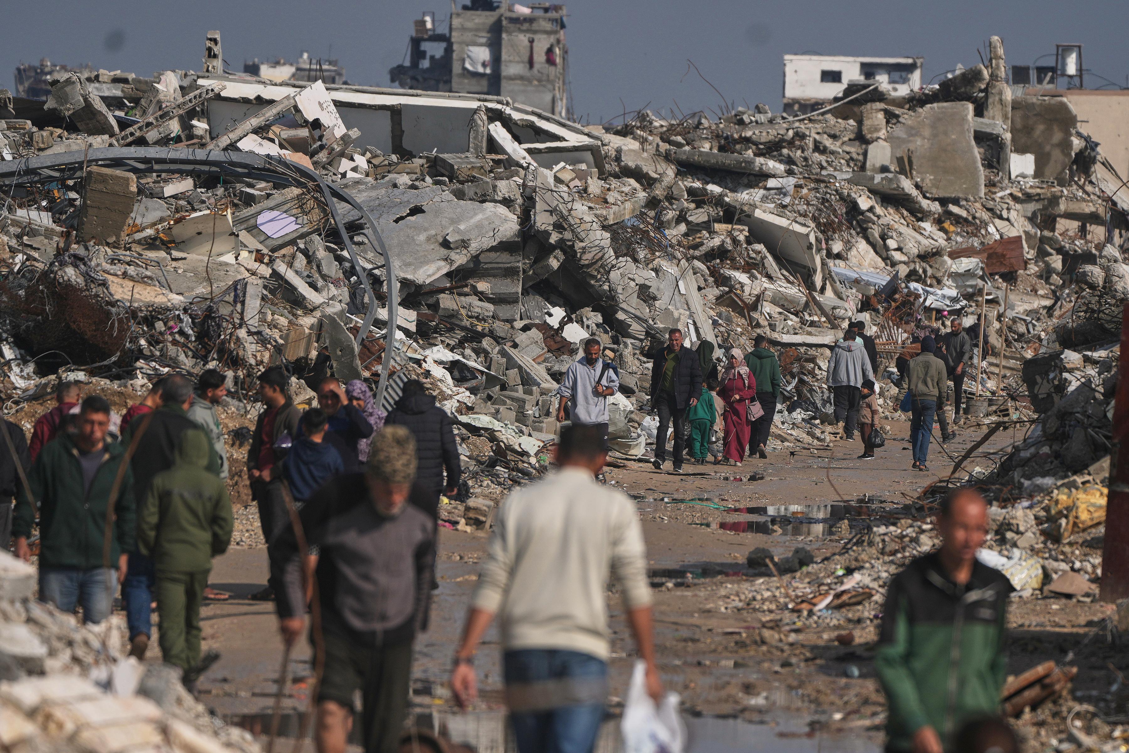 Palestinians walk by buildings destroyed during Israeli air and ground operations in Gaza City, December 17, 2025.