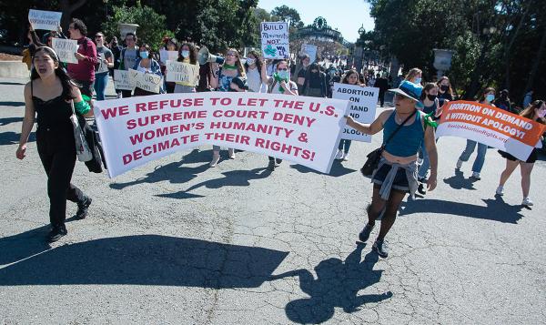 Berkeley march of hundreds behind bannner through campus on IWD.