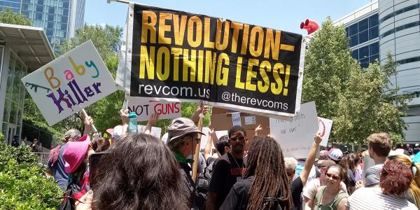 RevComs hold banner "Revolution—Nothing Less" at NRA convention in Houston.