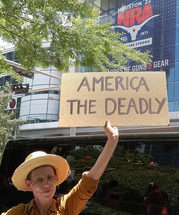 Protester holds "America Is Deadly" sign at NRA Houston.