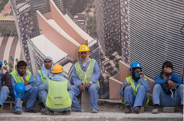 Construction workers in Qatar wait for a bus outside a construction site