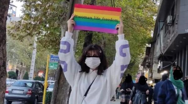 Woman in Iran holding pride flag that says "#woman_life_freedom"