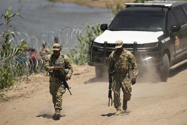 Guardsmen patrol as workers continue to place buoys and barbed wire as a border barrier, July 2023.