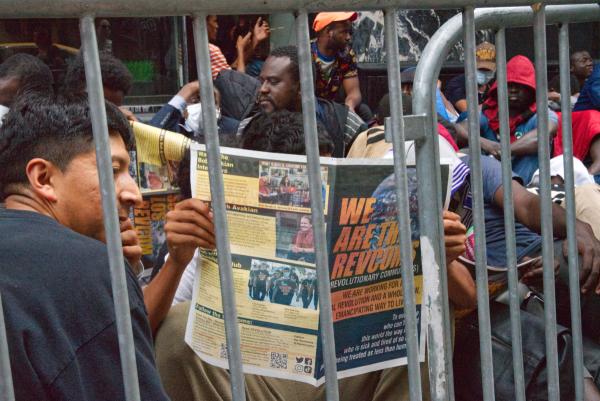 Migrants behind barricade at Roosevelt Hotel read proclamation, "We Are the Revcoms," August 1, 2023.