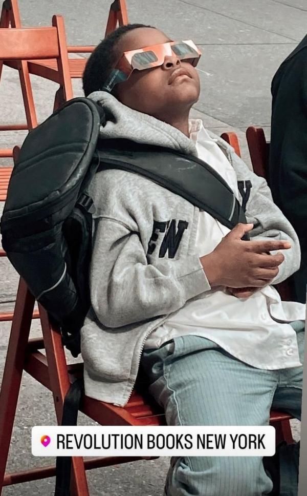 Outside of Revolution Books NYC, boy with eclipse glasses watching the eclipse.