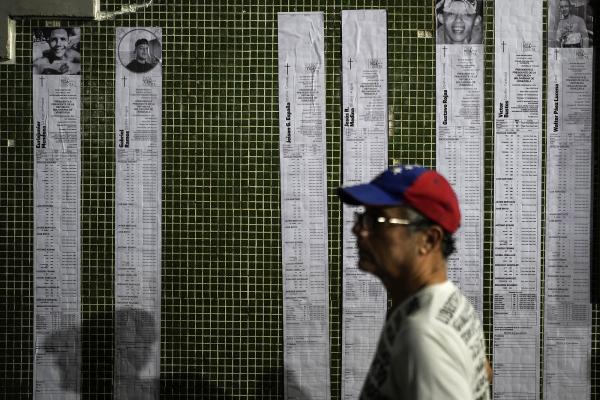 Venezuelan presidential election tallies, or "actas," stream down a wall with the faces of prisoners detained, August 8, 2024.