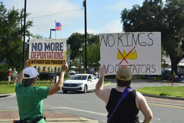 Two women hold up signs "No More Deportations without due process." "No Kings; No Dictators."