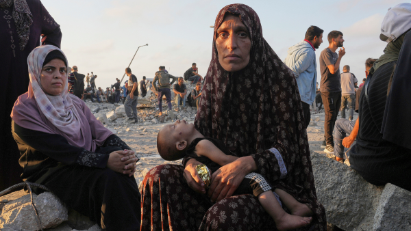 A starving Palestinian woman waits with her child for trucks with humanitarian aid to arrive in Gaza City, July 25, 2025.
