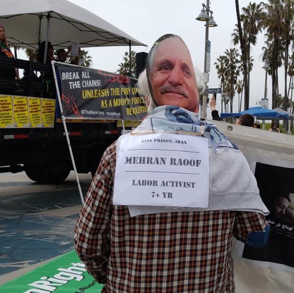 IEC volunteer wears mask of Mehran Raouf and “booking card” to highlight his case at International Women’s Day 2023 rally, Santa Monica, California.
