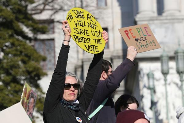 Woman holds up sign "The SAVE Act will not save us!! Protect the Vote.