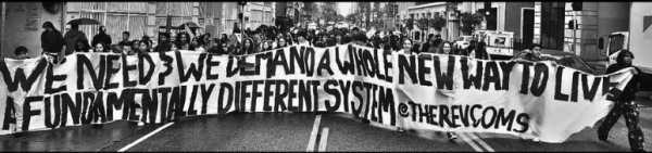 The Revcom Corps marching with banner: We Need and We Demand A Whole New Way To Live, A Fundamentally Different System