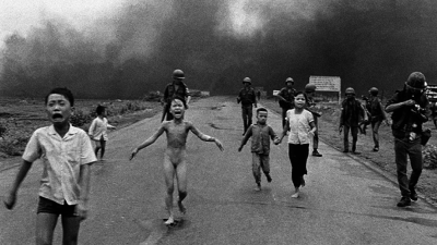 People severely burned from napalm attack run down the road.