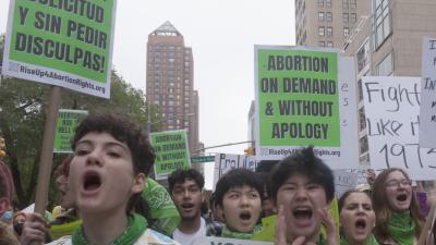 Young women marching with signs Abortion on Demand and Without Apology in English and Spanish