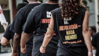 Back of woman marching with t-shirt that says ¡REVOLUCIÓN — NADA MENOS!