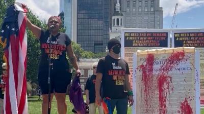 Revcoms holding the U.S. flag and red-paint-splattered constitution, July 4, in front of Independence Hall, Philadelphia.