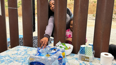 A woman seeking asylum reaches for a bottle of water after crossing the border with a child, June 5, 2024, in San Diego.