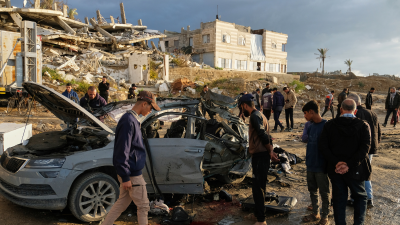 Palestinians look at a destroyed car following an Israeli strike in Gaza City, December 13, 2025