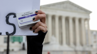 An abortion-rights activist holds a box of mifepristone pills as demonstrators from both anti-abortion and abortion-rights groups rally outside the Supreme Court in Washington, March 26, 2024.