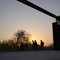 People waiting to cross border silhouetted against sky at gap in border wall Texas