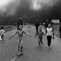 People severely burned from napalm attack run down the road.