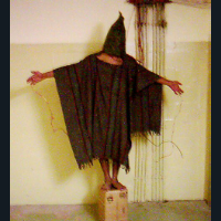 , a hooded Iraqi is shown balanced on small box, with wires attached to his fingers—he was forced to stand for hours, told that if he fell over from exhaustion, the wires would electrocute him