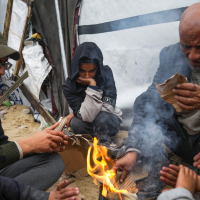 Displaced Palestinians warm by a fire at a camp near Rafah, Gaza, February 24, 2025.
